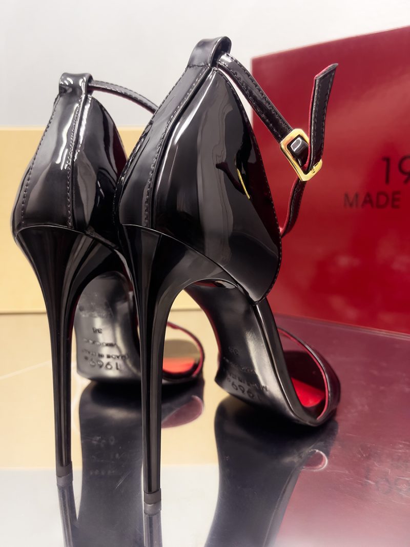 Rear view of black patent leather stiletto sandals highlighting the slender high heels and gold buckle.