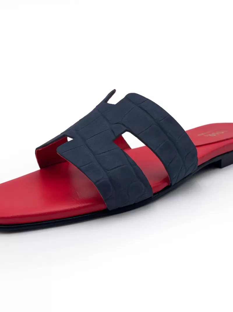 Side view of 1969 dark blue croc-embossed suede flat slide sandal with contrasting red leather footbed.