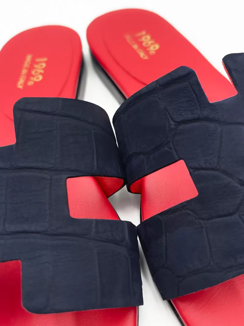 Close-up of dark blue croc-embossed suede flat sandals showing H-strap and gold Made in Italy stamp on red insole.