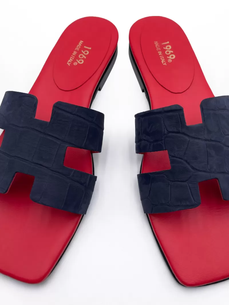Top-down view of 1969 dark blue croc-embossed suede flat slide sandals with red footbed and gold logo.