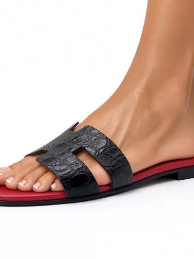 Side view of a model wearing an Oran black croc-embossed leather flat sandal with H-cut strap and red footbed.