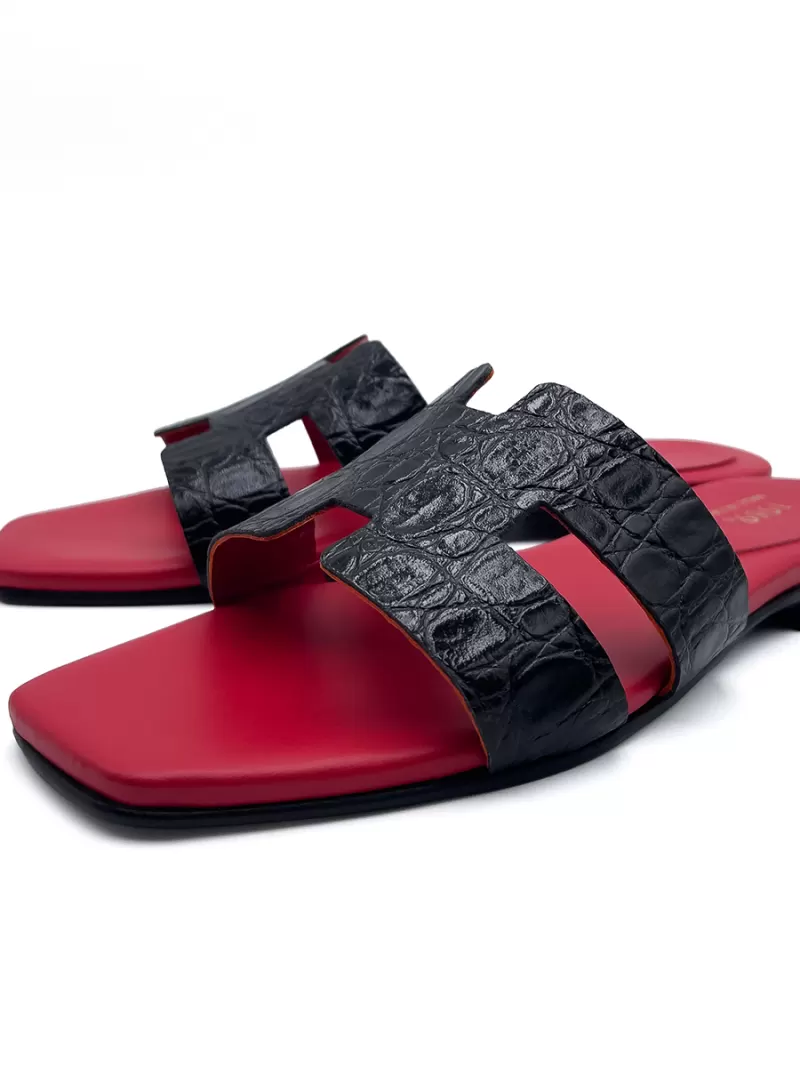 Studio view of 1969 Oran black croc-embossed leather flat sandals with H-straps, red footbeds, and square toes.