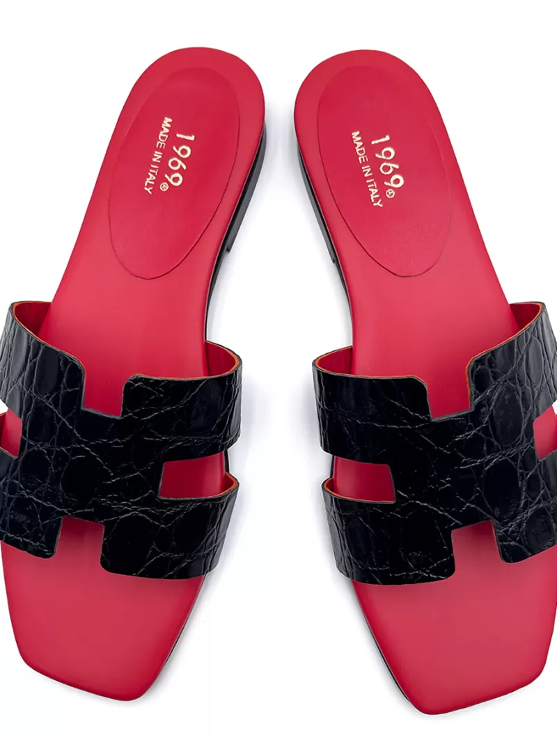 Top-down view of 1969 Oran black croc-embossed leather flat sandals featuring signature red footbeds and H-cut straps.