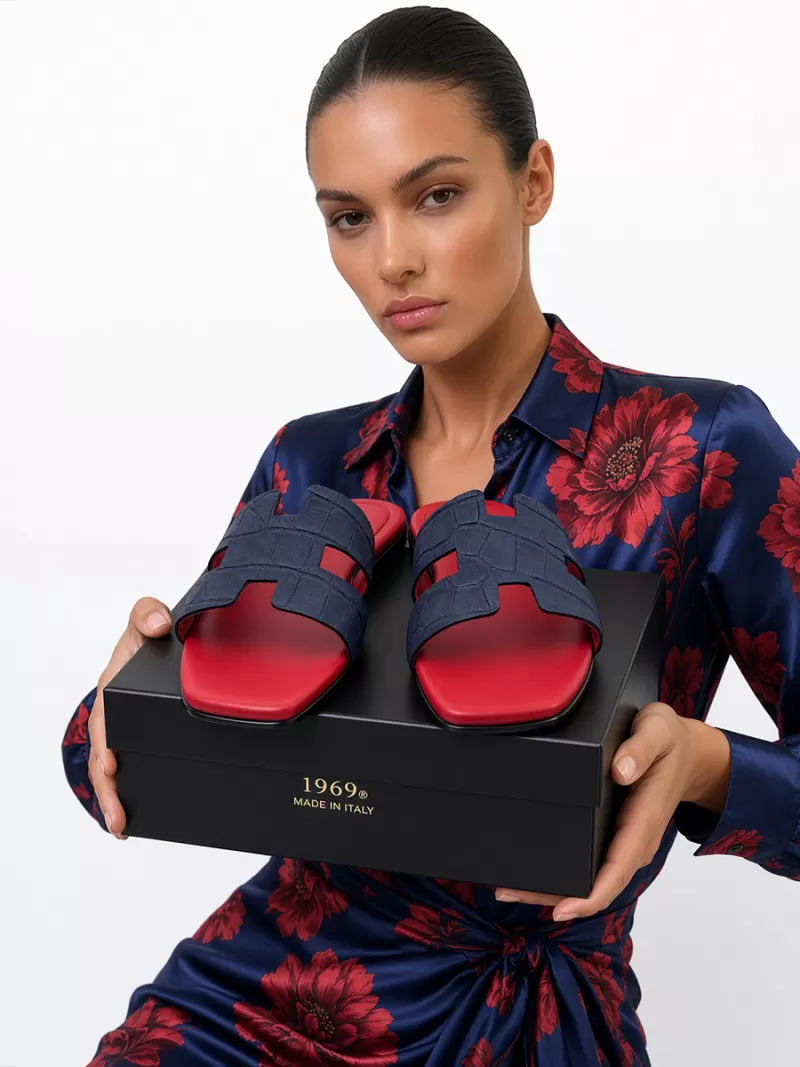 Model holding Oran blue croc-embossed suede leather flat sandals with red footbeds on a black 1969 Made in Italy shoe box.