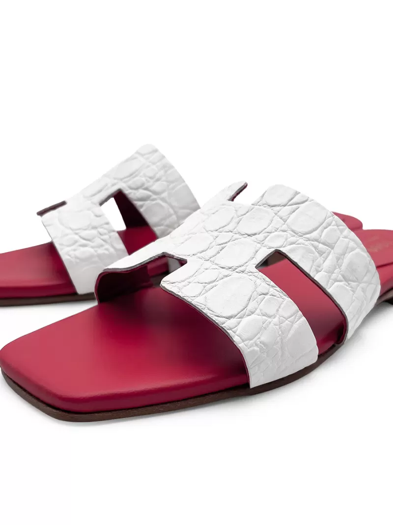 Angled front view of Oran white croc-embossed leather flat sandals with H-cut uppers, square toes, red footbeds and brown soles.