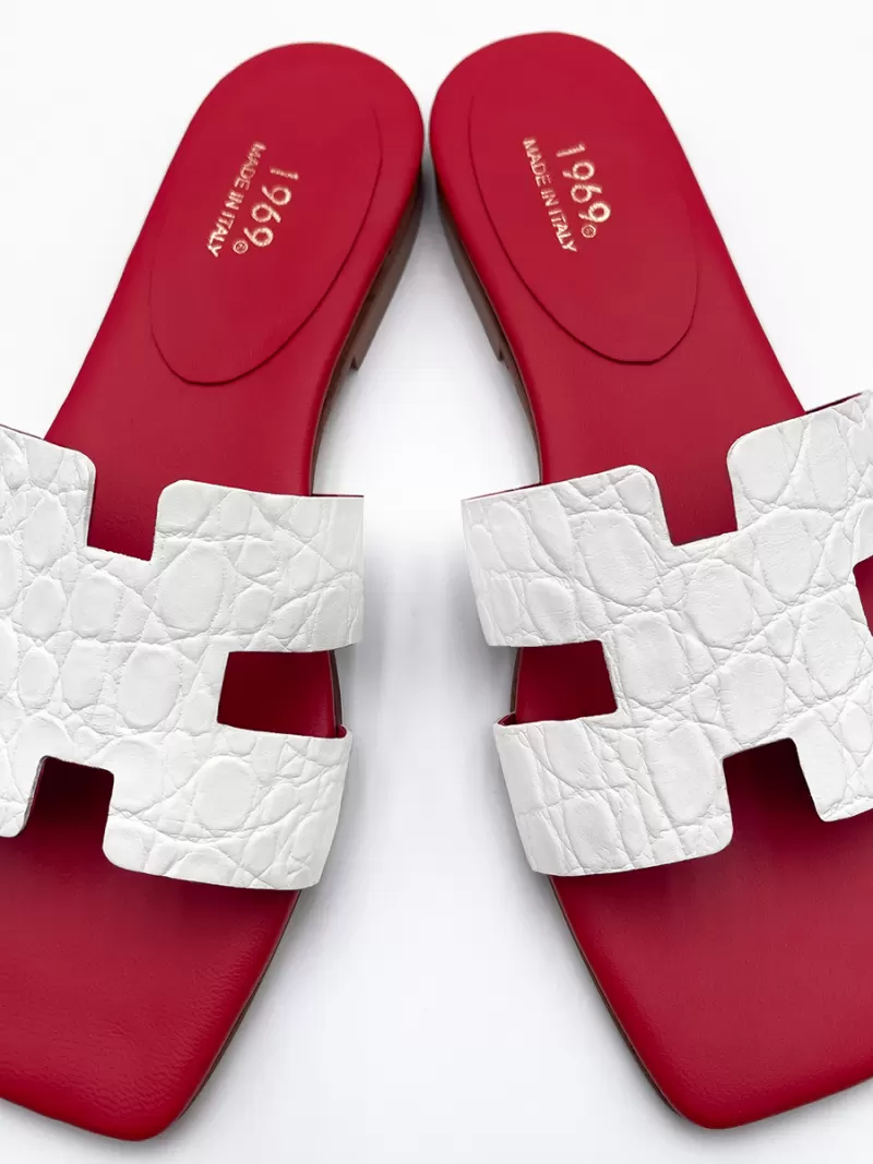 Top view of Oran white croc-embossed leather flat sandals with H-cut uppers, square toes and red footbeds with gold branding.