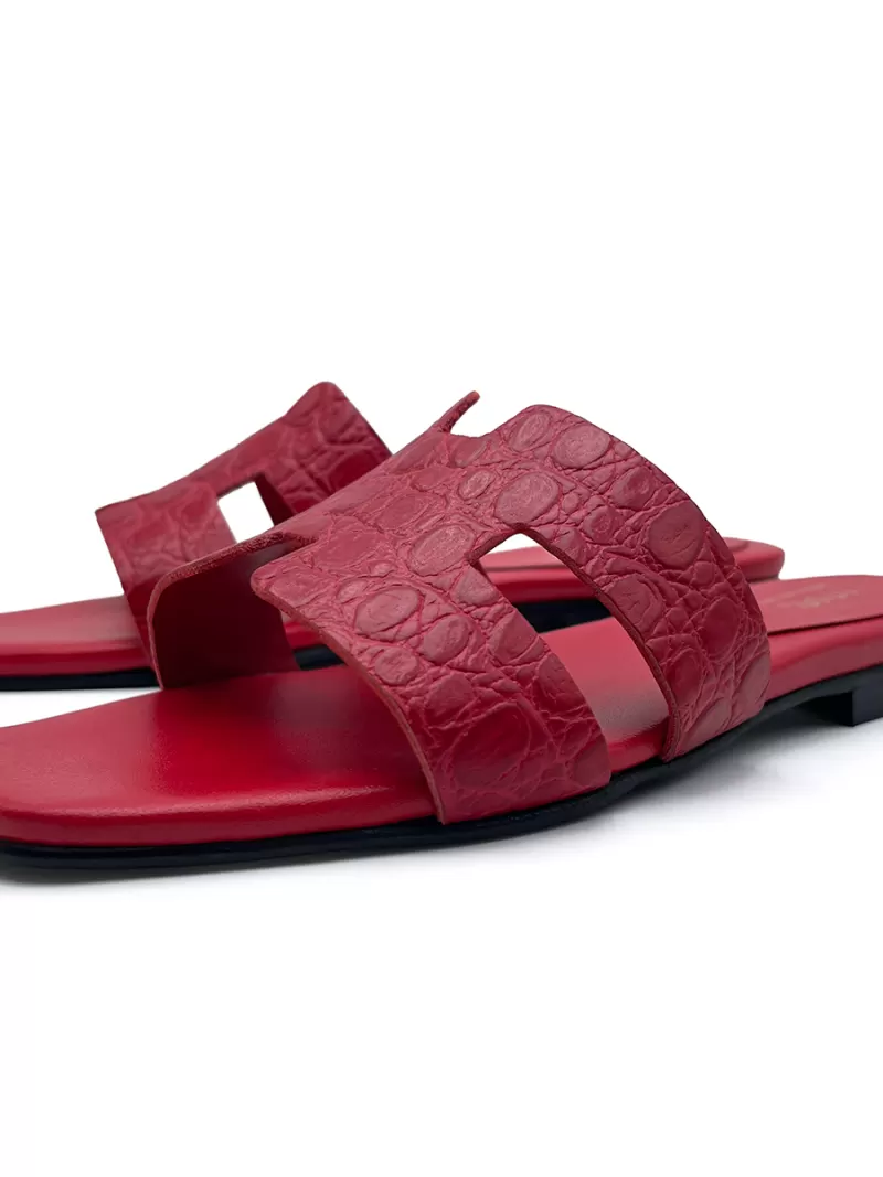 Staggered front-side view of 1969 red croc-embossed leather flat slide sandals with H-strap.