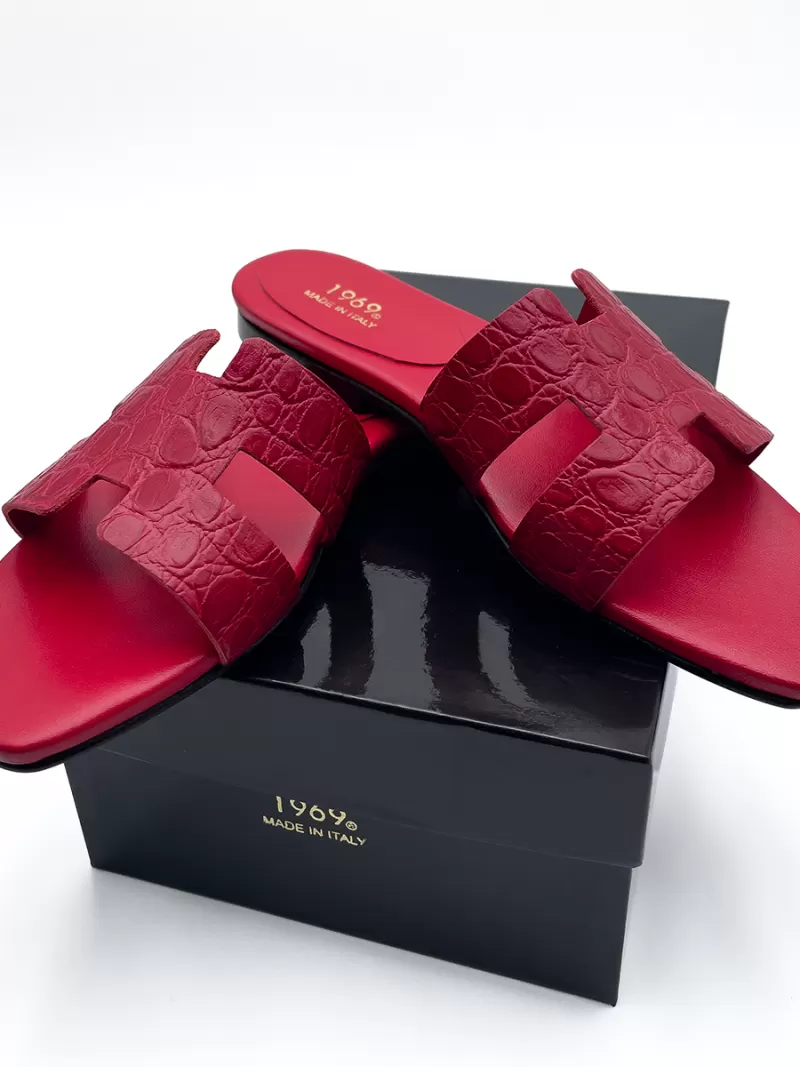 1969 red croc-embossed leather flat slide sandals displayed on top of a black box with gold logo.