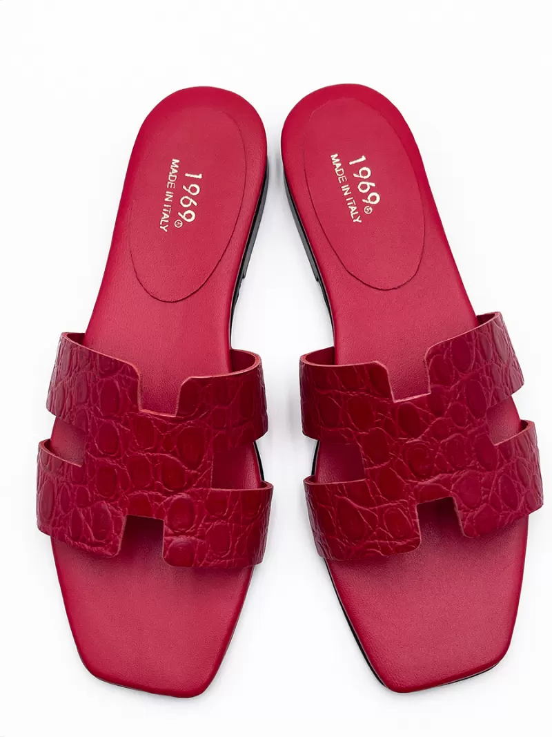 Top-down view of 1969 red croc-embossed leather flat slide sandals with H-strap and gold stamped footbed logo.