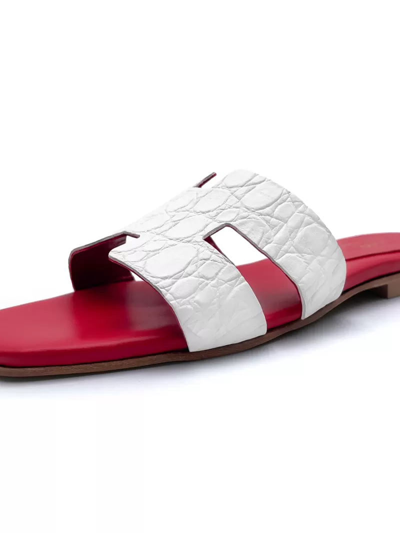 Angled side profile of a white croc-embossed leather flat slide sandal with a square toe and red footbed.