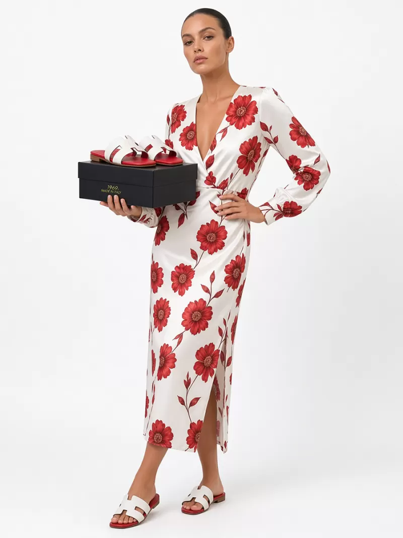 Model in floral dress wearing white croc leather flat sandals and holding a black shoe box.